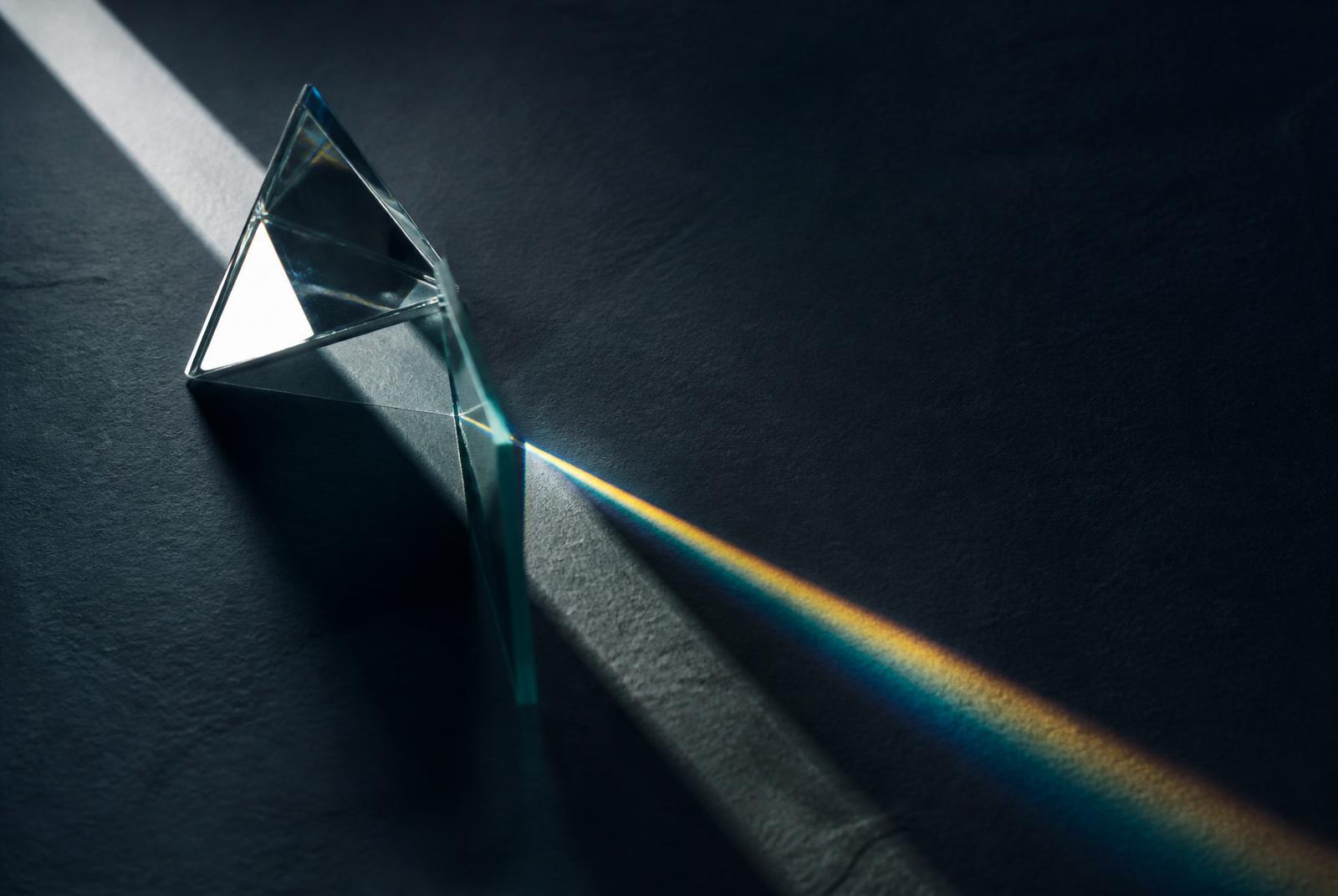Glass prism separating a beam of light across a dark slate surface